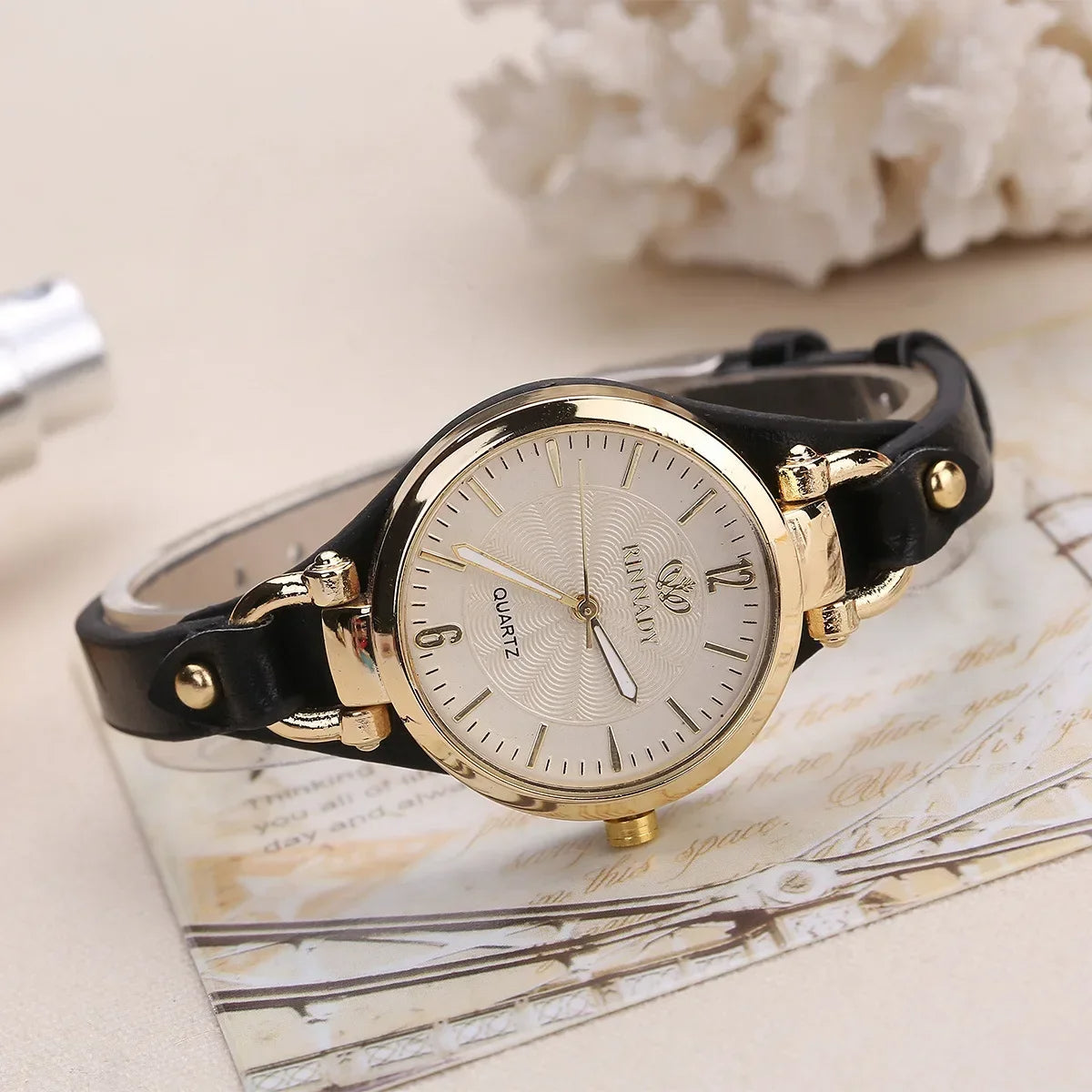 Gold watch with black leather strap on a decorative surface