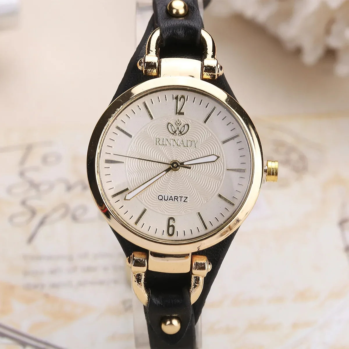 Wristwatch with gold case and black strap on a textured background