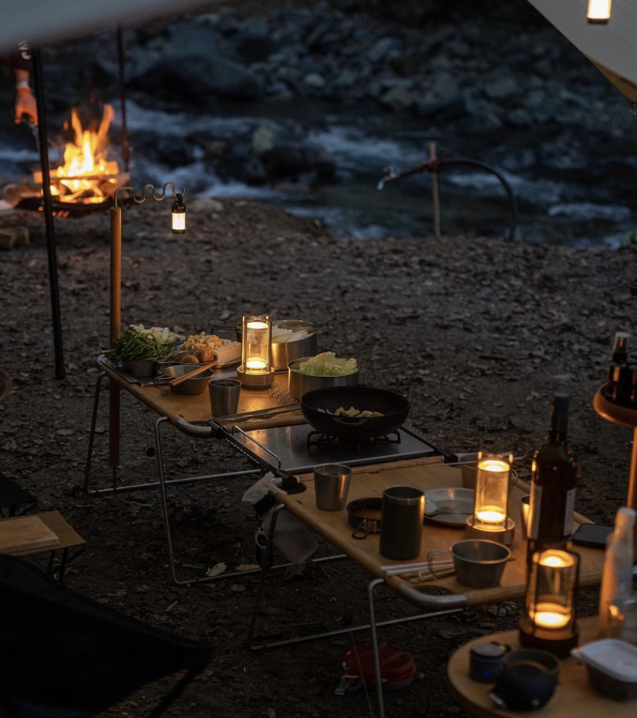 Evening beach picnic with candles, food, and drinks by a campfire.