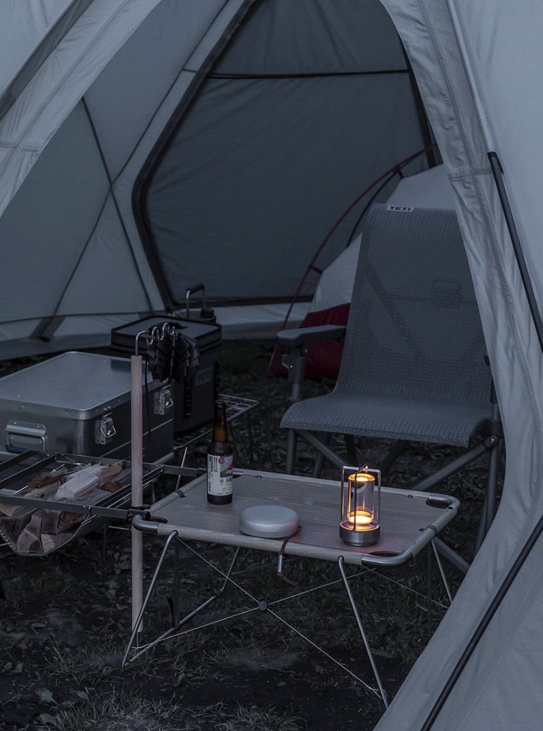Camping scene with a tent, chair, and small table with a bottle and lantern inside.