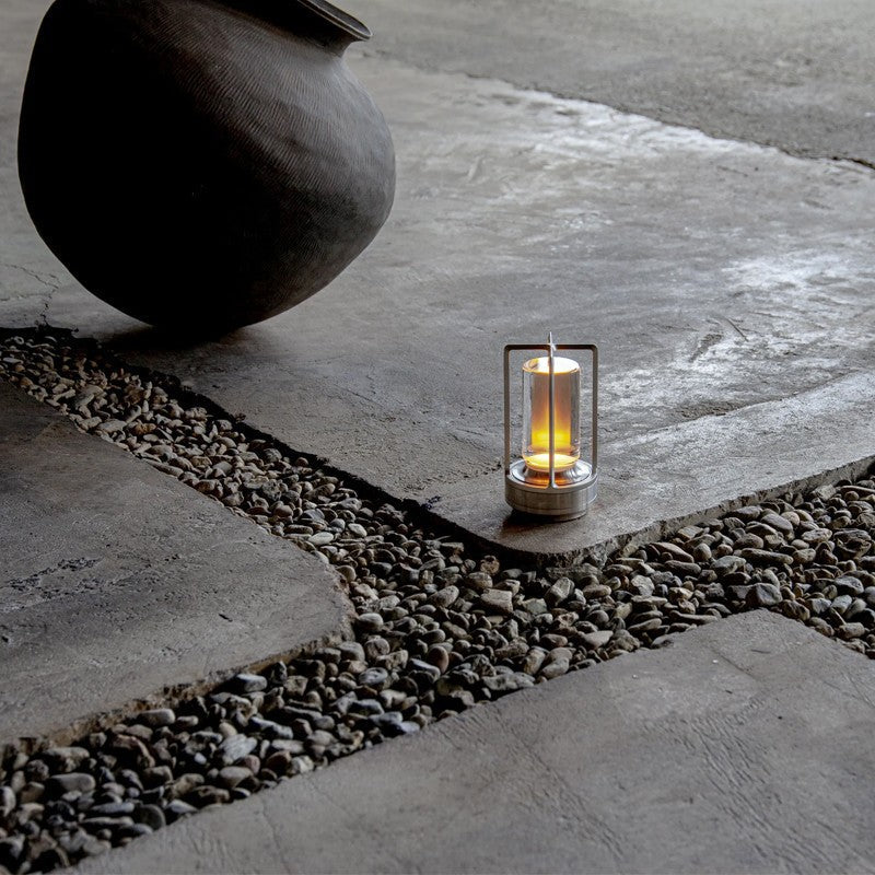 Candle in a metal lantern on a stone pathway with a large stone pot nearby.
