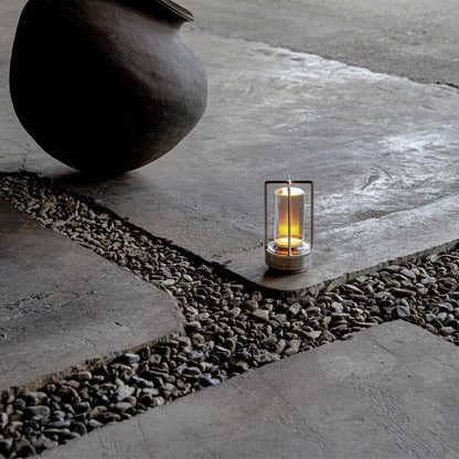 Candle in a metal lantern on a stone pathway with a large stone pot nearby.