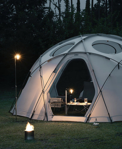 Camping scene with a dome tent, lanterns, and a small table setup at night.