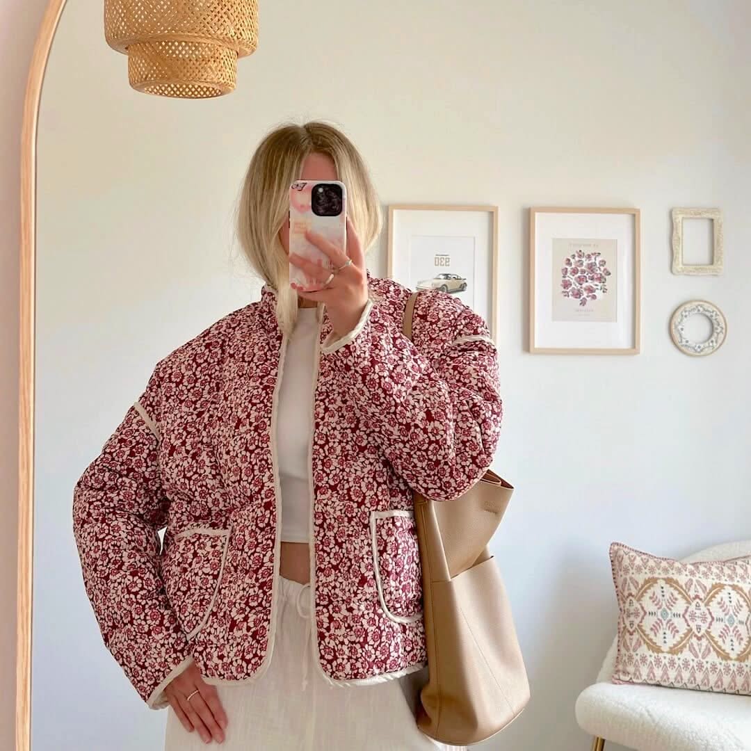 Person wearing a red floral jacket in a room with framed pictures on the wall.