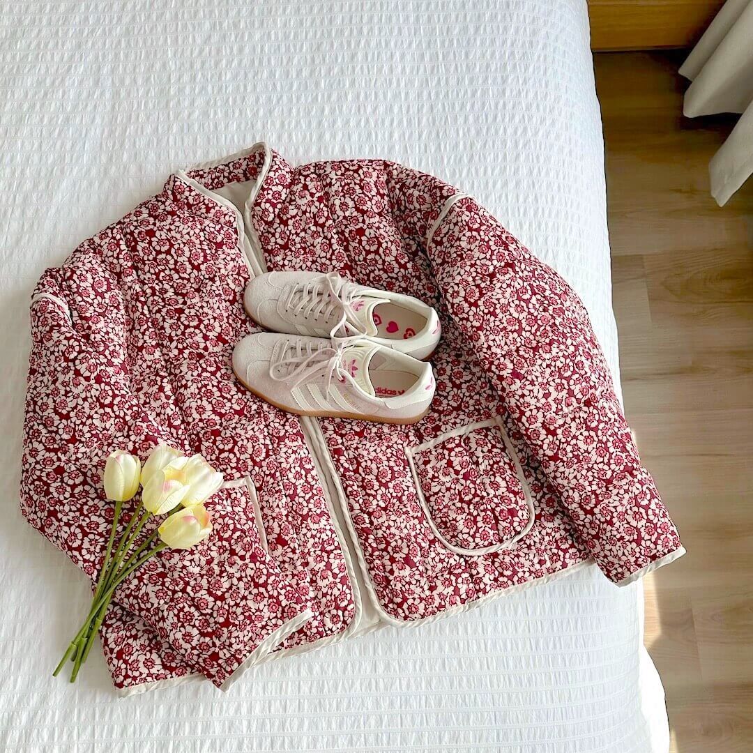 Floral-patterned jacket on a bed with white sneakers and yellow flowers.