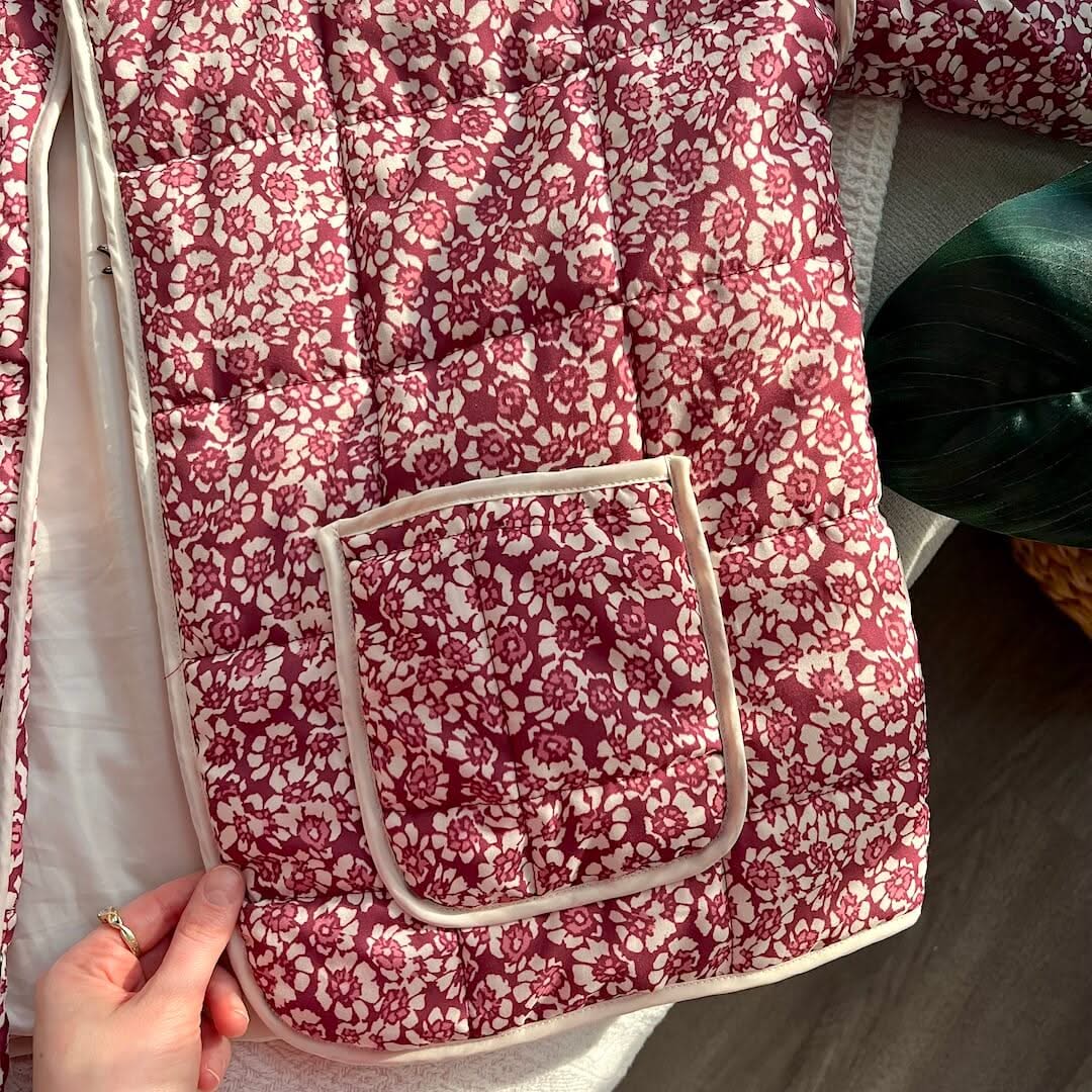 Red floral-patterned fabric with a pocket held by a hand on a neutral background