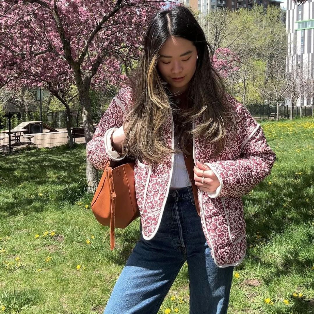 Woman in a floral jacket standing in a park with cherry blossom trees