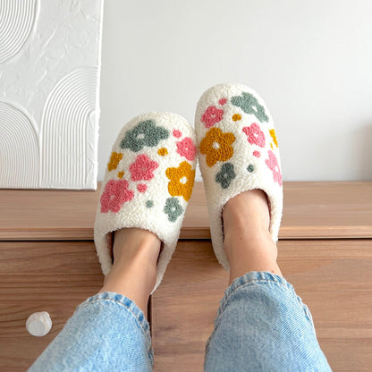 Floral patterned slippers worn with light blue jeans on a wooden floor.
