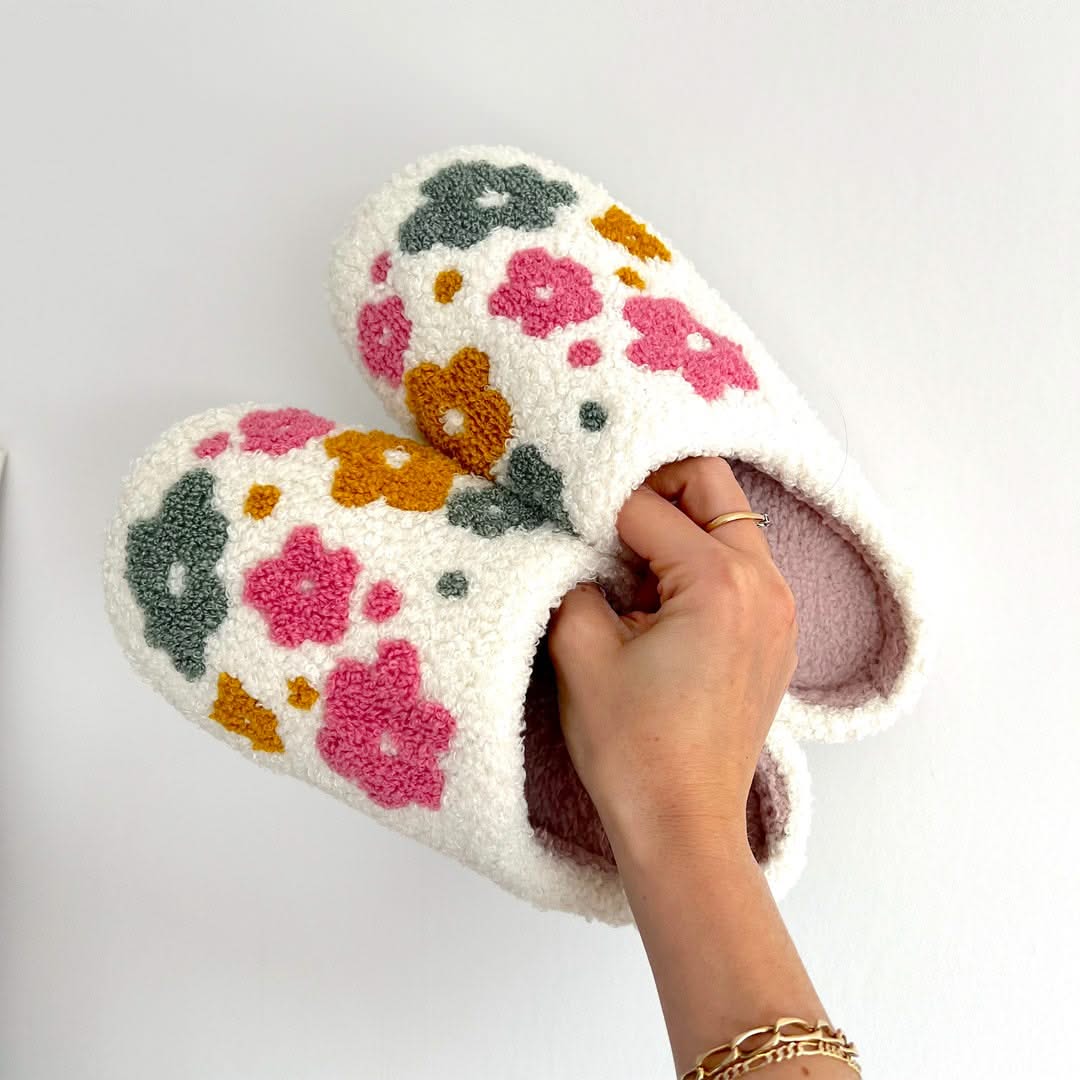Floral-patterned slippers being held by a hand on a light gray background
