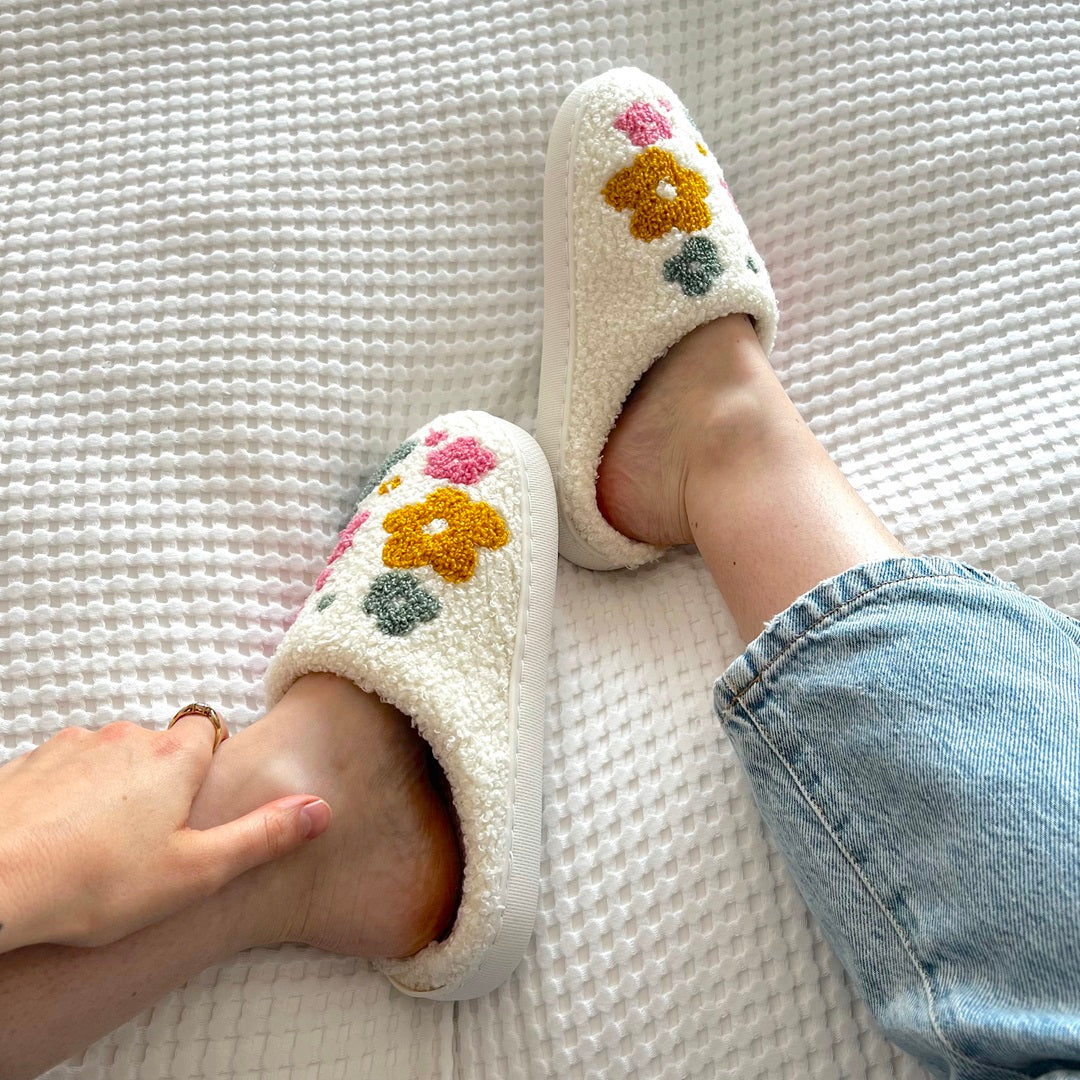 White slippers with floral designs worn by a person on a textured surface.