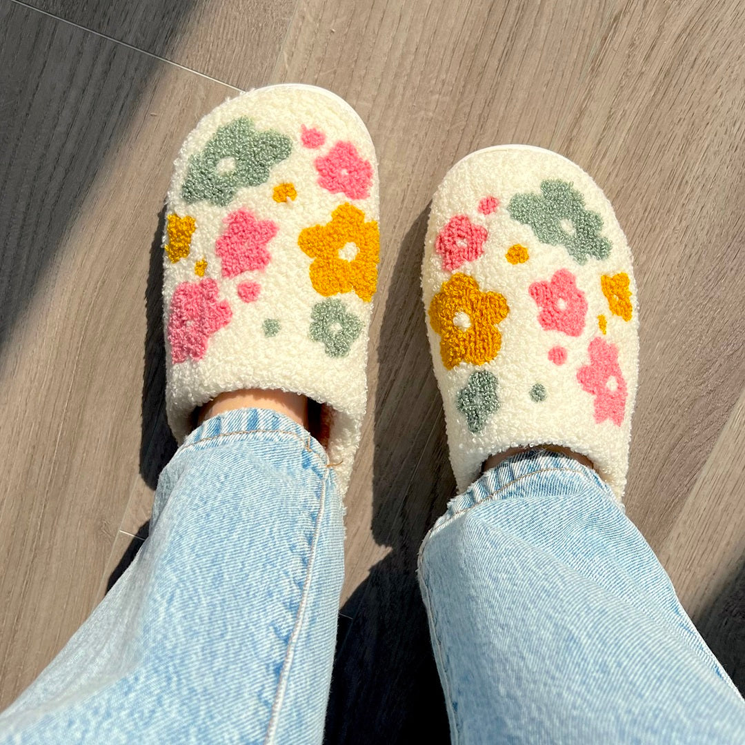 Floral patterned slippers worn with light blue jeans on a wooden floor.