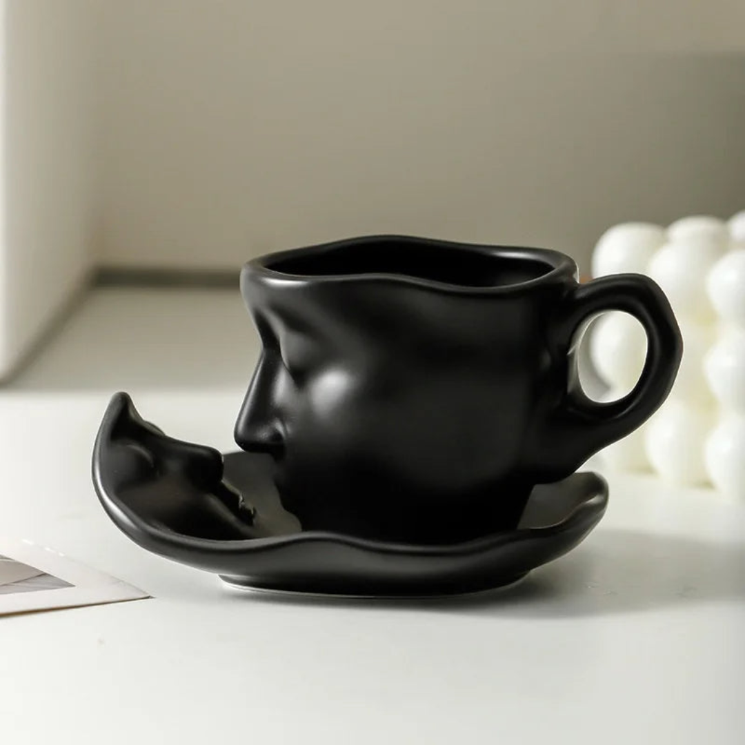 Black ceramic face-shaped cup and saucer on a light surface.