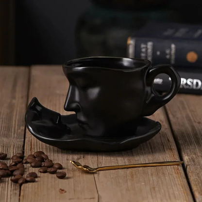 Black ceramic face-shaped coffee cup and saucer on a wooden surface with coffee beans and a spoon.