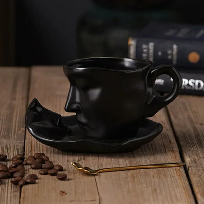 Josh & Tate - Lover's Gaze Reverie Coffee Ceramic Mug - Black ceramic cup and saucer shaped like a face on a wooden table with coffee beans and a spoon.