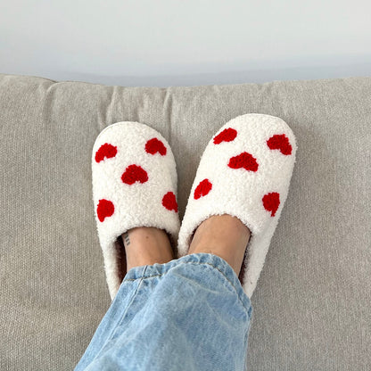White slippers with red polka dots worn on a gray couch.