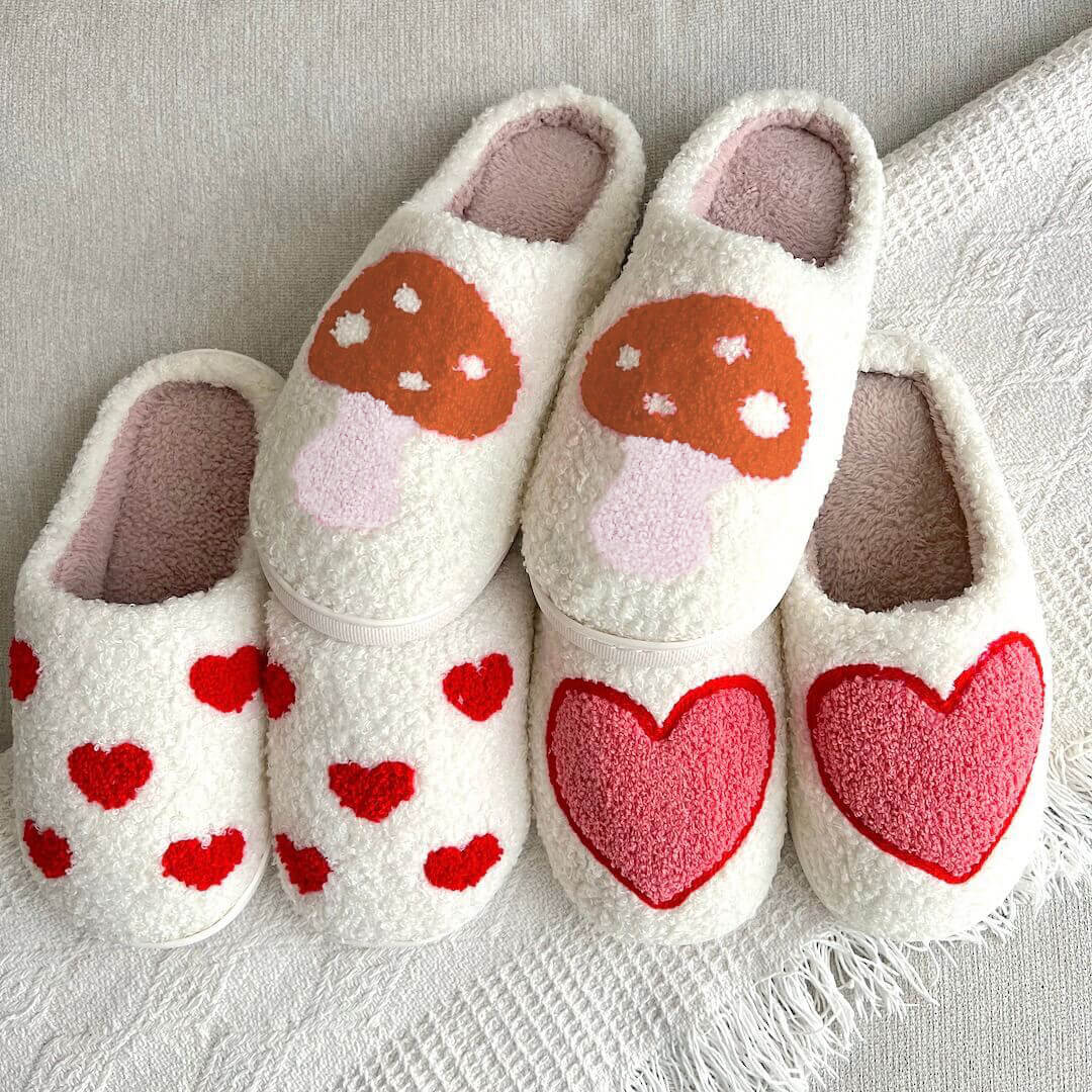 Pair of white slippers with red heart designs on a textured surface