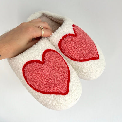 White slippers with red heart designs held by a hand on a light gray background