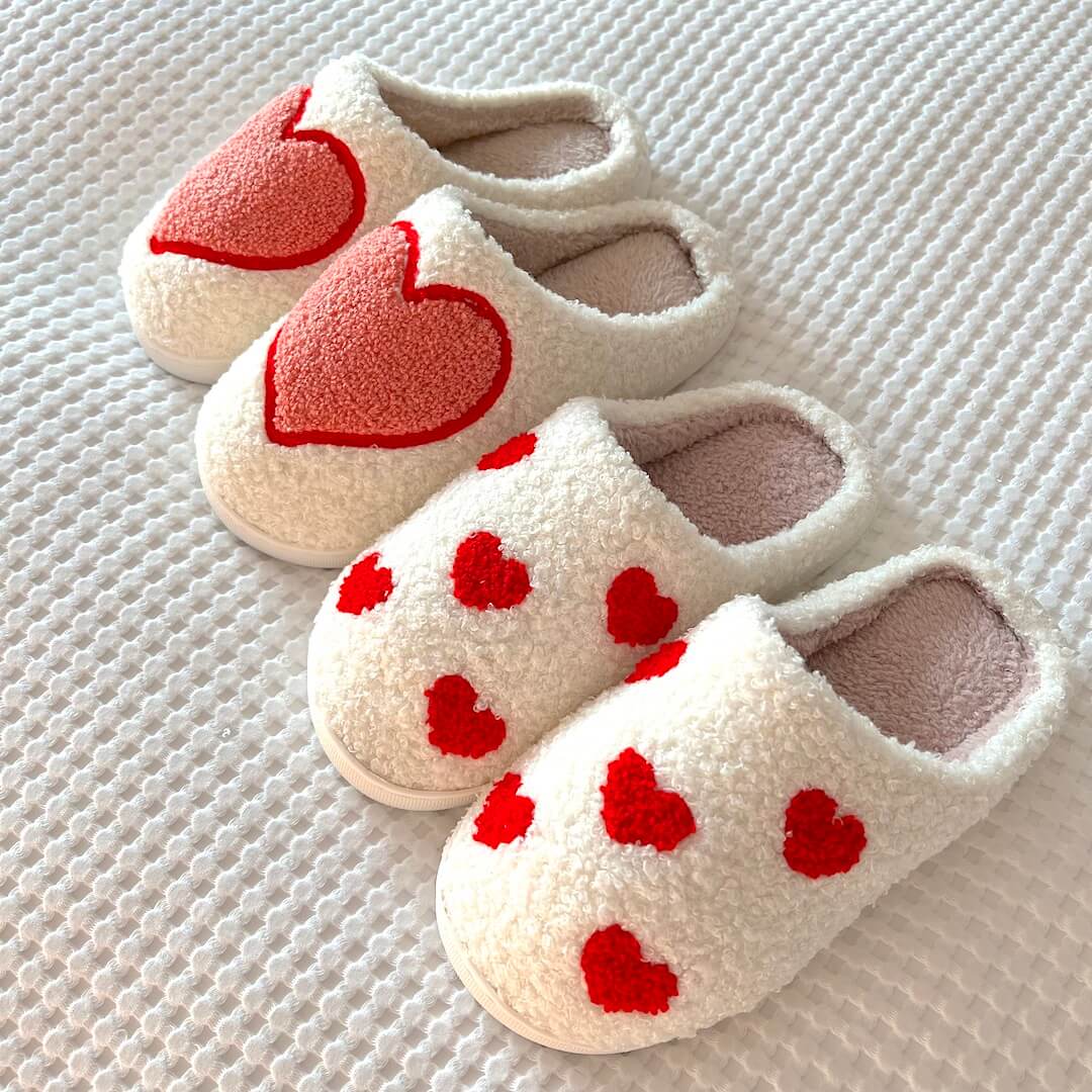 Pair of white slippers with red heart designs on a textured surface