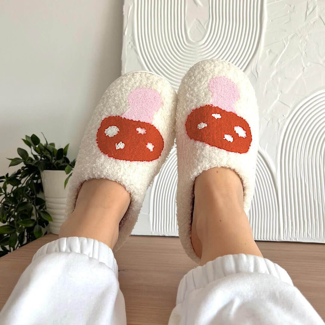 White fuzzy slippers with red mushroom design worn indoors.
