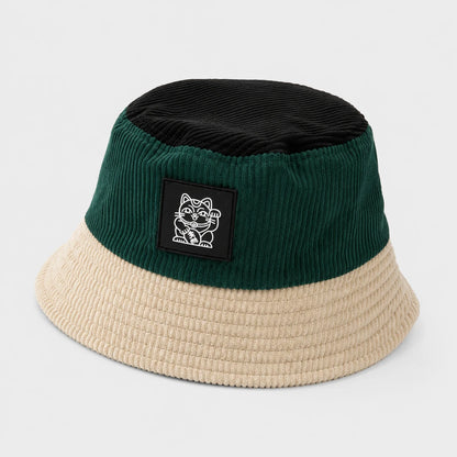 Josh & Tate - LuckyBrim™ Colorblock Bucket Hat - A two-tone corduroy bucket hat with a dark green crown, a black top panel, and a beige brim, featuring a black rectangular patch with a white cartoon cat logo on the front.