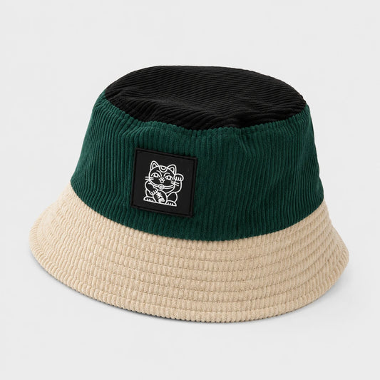 Josh & Tate - LuckyBrim™ Colorblock Bucket Hat - A two-tone corduroy bucket hat with a dark green crown, a black top panel, and a beige brim, featuring a black rectangular patch with a white cartoon cat logo on the front.