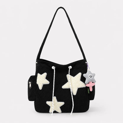 Josh & Tate - LuckyStar™ Ribbed Tote Bag - A black corduroy shoulder bag decorated with three white glittery star appliqués, white drawstrings, a side zip pocket, and a small gray plush star charm with a pink bow, shown against a light gray background.