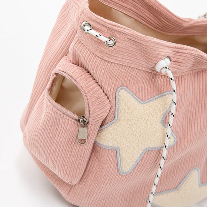 Josh & Tate - LuckyStar™ Ribbed Tote Bag  - A close-up of a dusty pink corduroy tote bag featuring a large cream-colored star applique with a gray outline on the front pocket, a zippered side pocket, and white drawstring cords with black speckles.