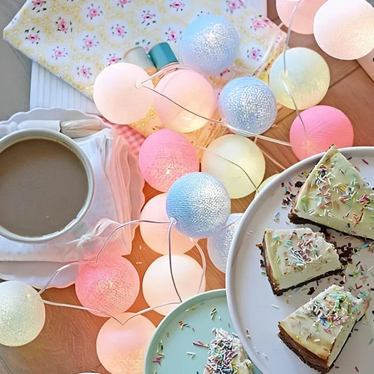 String lights with pastel colors over a table setting with a cup of coffee and slices of cake.