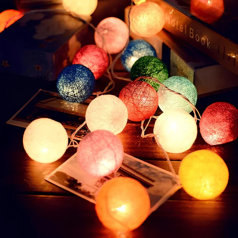 String of colorful cotton ball lights on a wooden surface with a blurred background.