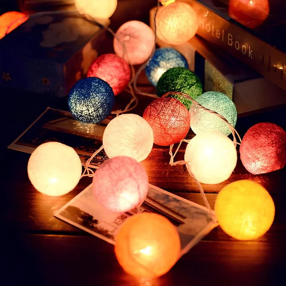String of colorful cotton ball lights on a wooden surface with a blurred background.