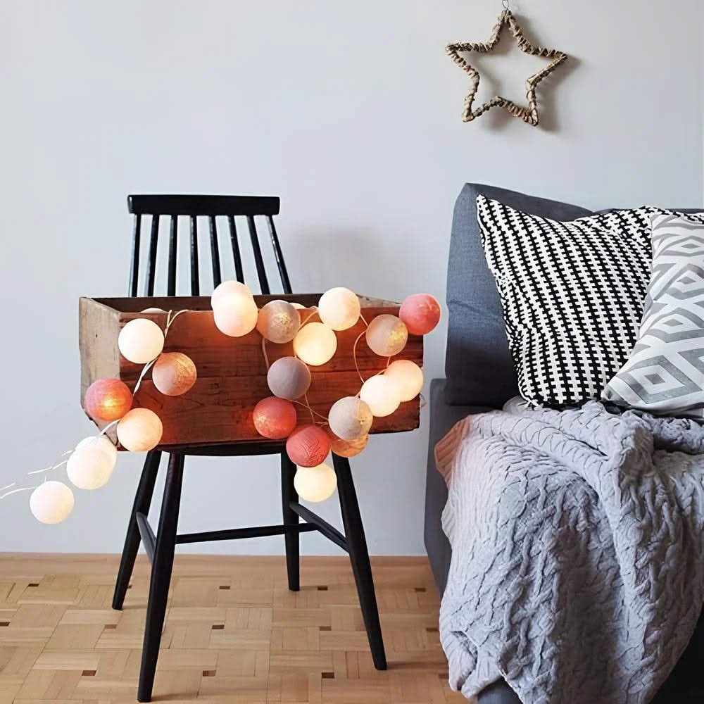 String lights on a wooden stool next to a bed with pillows and a blanket.