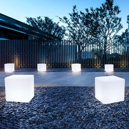 White cubic light fixtures on a gravel surface with trees and a building in the background.