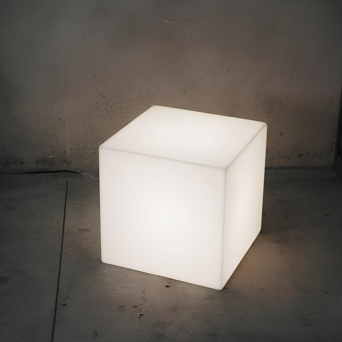Cube-shaped illuminated lamp on a concrete floor with a dark background