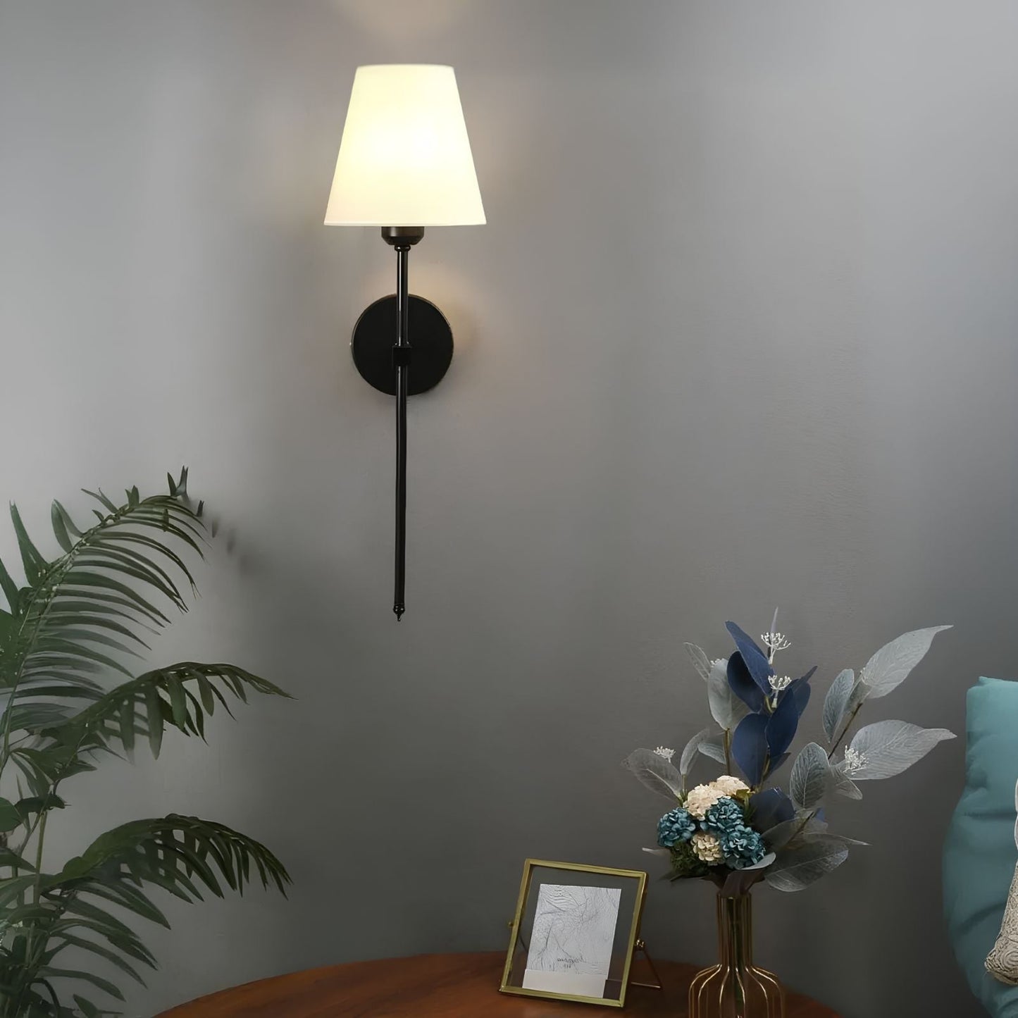 Wall-mounted lamp with a plant and decorative items on a table against a gray wall.