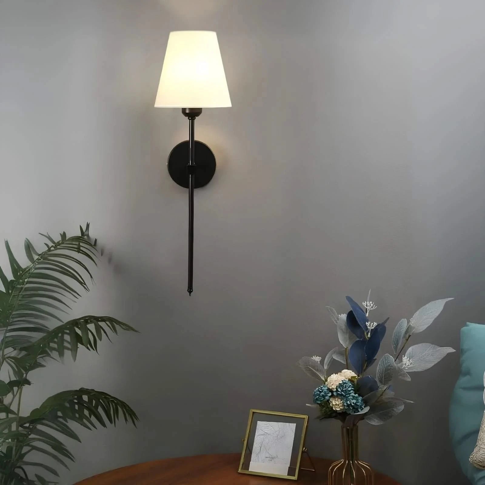 Josh & Tate - LumaElegance Wireless Wall Lamp - Wall-mounted lamp with a plant and decorative items on a table against a gray wall.