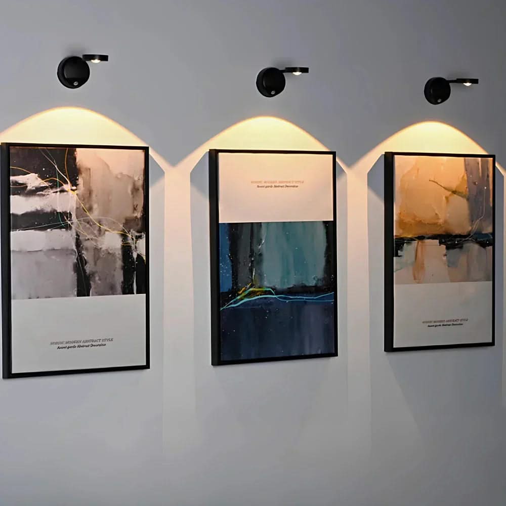 Three framed artworks on a wall with lighting fixtures above.