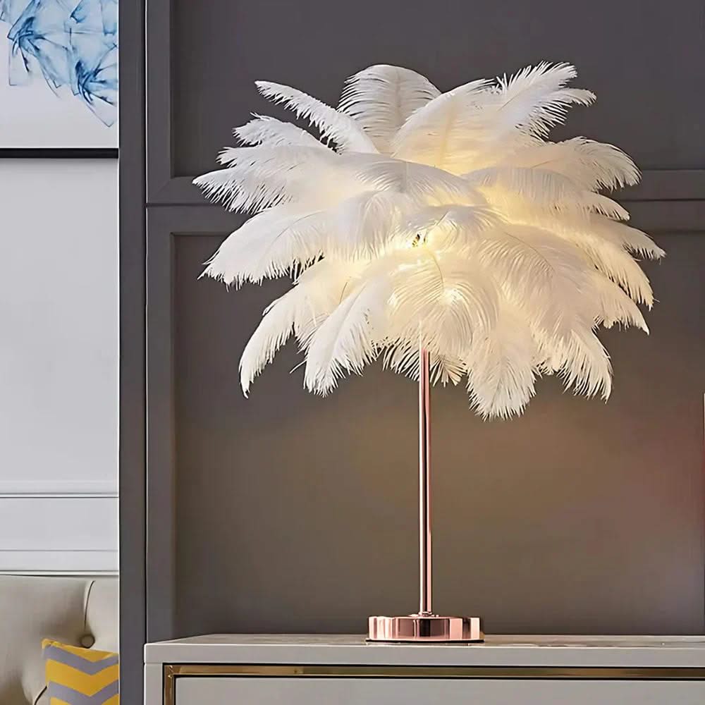 Feathered table lamp with a rose gold base on a shelf against a gray wall.