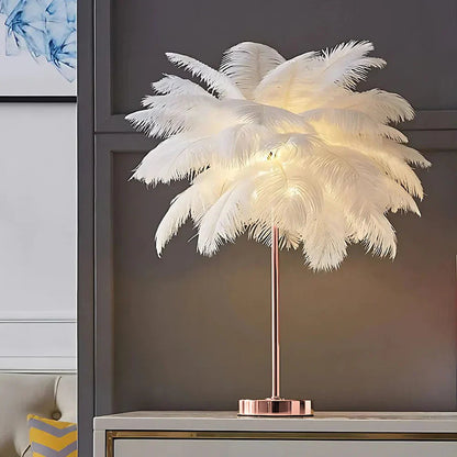 Feathered table lamp with a rose gold base on a shelf against a gray wall.