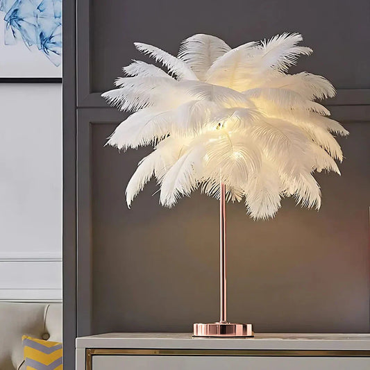 Feathered table lamp with a rose gold base on a shelf against a gray wall.