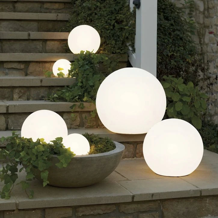 Josh & Tate - LumaSphere Wireless Mood Lamp - Glowing spherical outdoor lights on a stone ledge with plants.