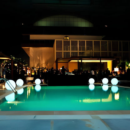 Pool area with illuminated balloons at night, people around, and building in the background.