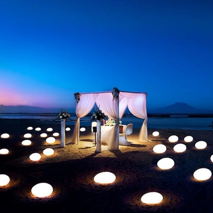 Romantic beach setting with a decorated canopy and candles on the sand at night.