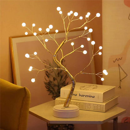 Decorative LED tree lamp on a small table with books in a cozy room setting.