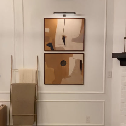 Two abstract wall art pieces on a neutral wall with a towel rack and light fixture.
