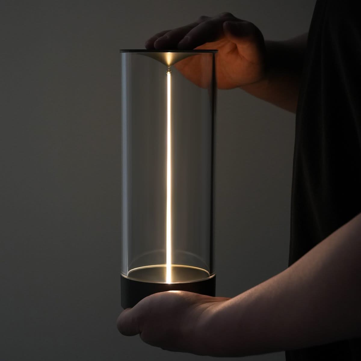 Person holding a cylindrical light fixture with a glowing interior against a dark background