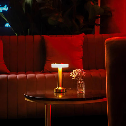 Red couch with a small table holding a lamp and a glass of water in a dimly lit room.