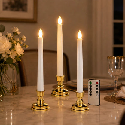 Josh & Tate - LumiCandle Standing LED Light - Three lit white taper candles in gold candlesticks on a dining table, with a small remote control beside them in a warmly lit indoor setting.