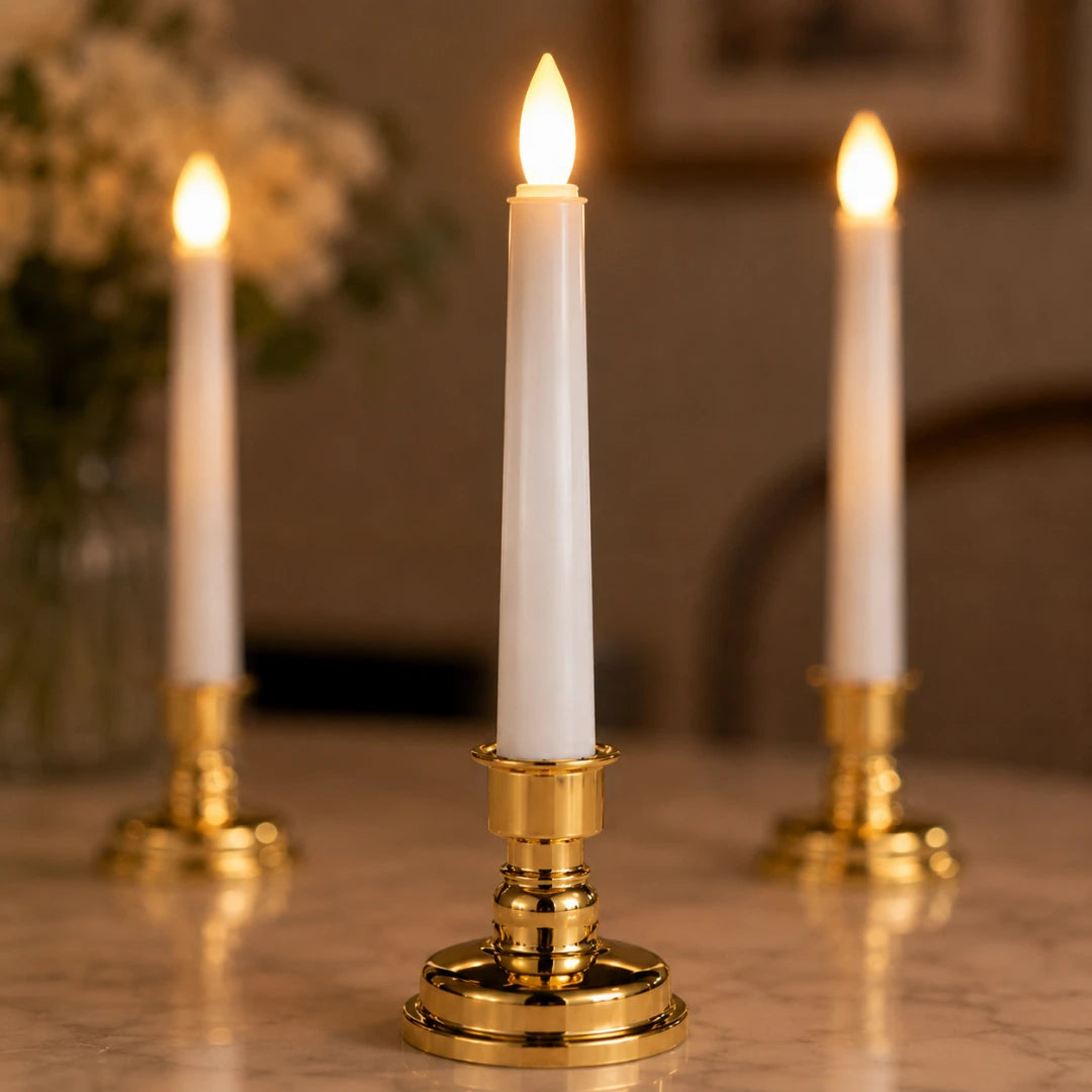 Josh & Tate - LumiCandle Standing LED Light - Three white taper candles in polished gold candlesticks, with the center candle lit and in sharp focus while the two rear candles are softly blurred in the background on a tabletop.