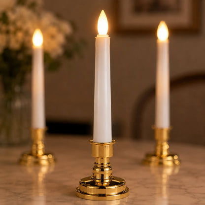 Josh & Tate - LumiCandle Standing LED Light - Three white taper candles in polished gold candlesticks, with the center candle lit and in sharp focus while the two rear candles are softly blurred in the background on a tabletop.