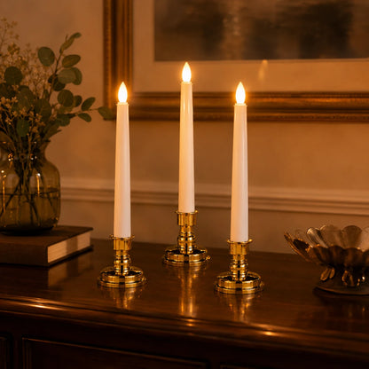 Josh & Tate - LumiCandle Standing LED Light - Three lit white taper candles in ornate gold candlesticks displayed on a dark wooden table in a warmly lit room.